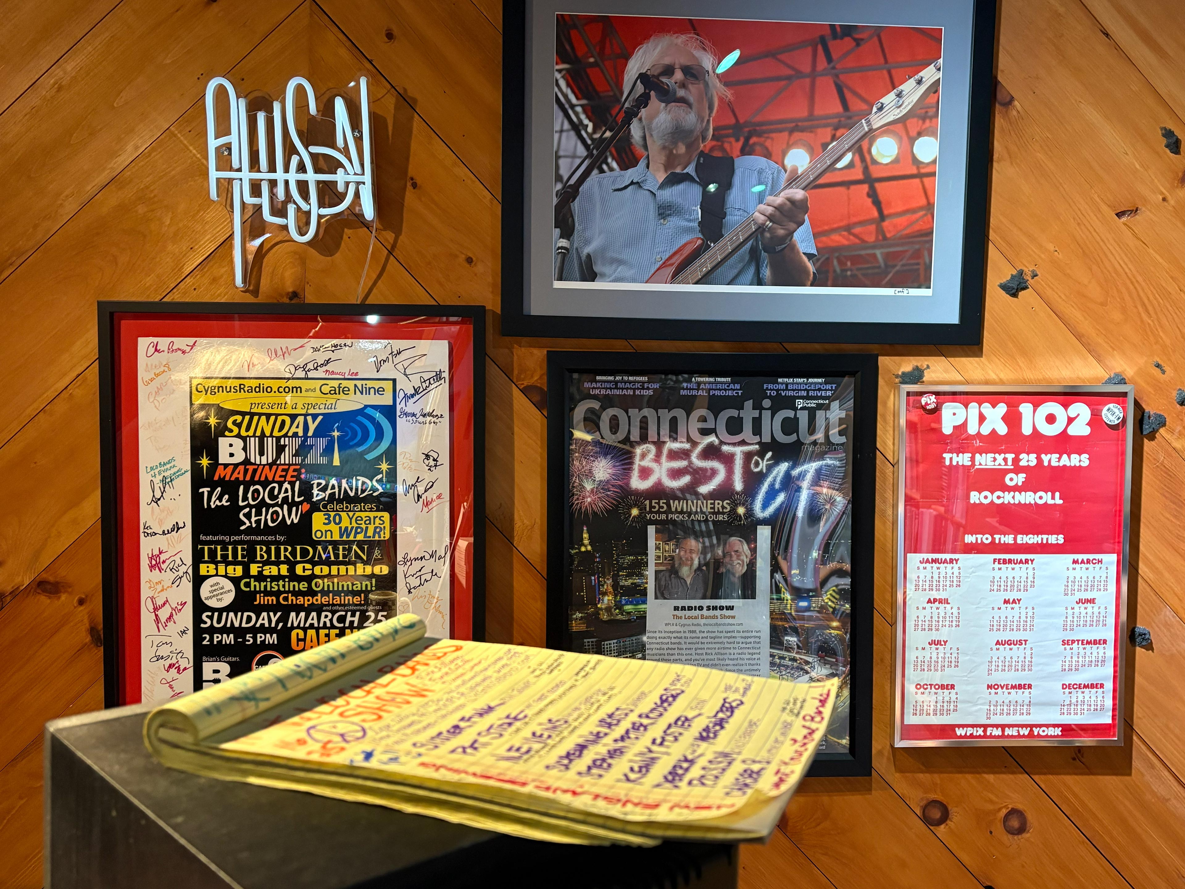 Wood slat wall with The Local Bands Show memorabilia including accolades, advertisements, show schedule and more